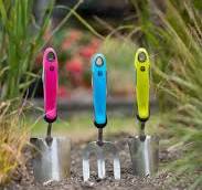 Three garden hand tools have been suck into the ground, their handles are bright pink, turquoise and yellow.