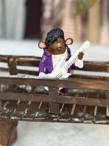 A mouse is standing on a bridge and is holding a white guitar